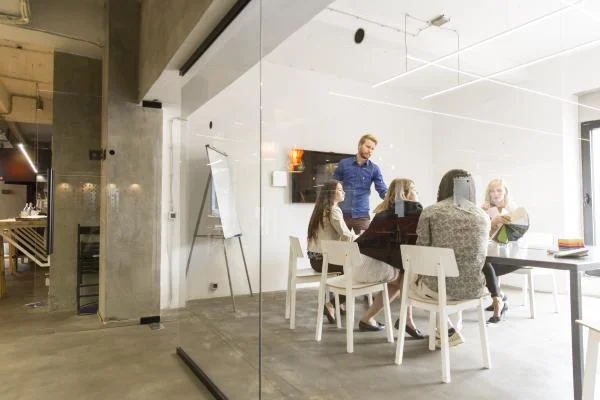 group of people sitting in room with glass walls with tv and paper presentation board